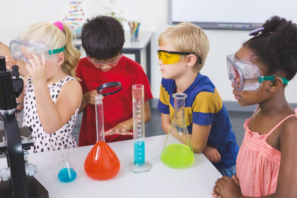50 acertijos de ciencia que te dejarán rascándote la cabeza Cuatro niños con gafas de seguridad haciendo un experimento científico.
